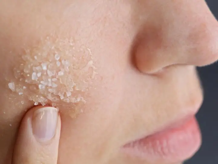 Dito, un dito applica un peeling acido glicolico a casa, con cristalli visibili sulla pelle.
