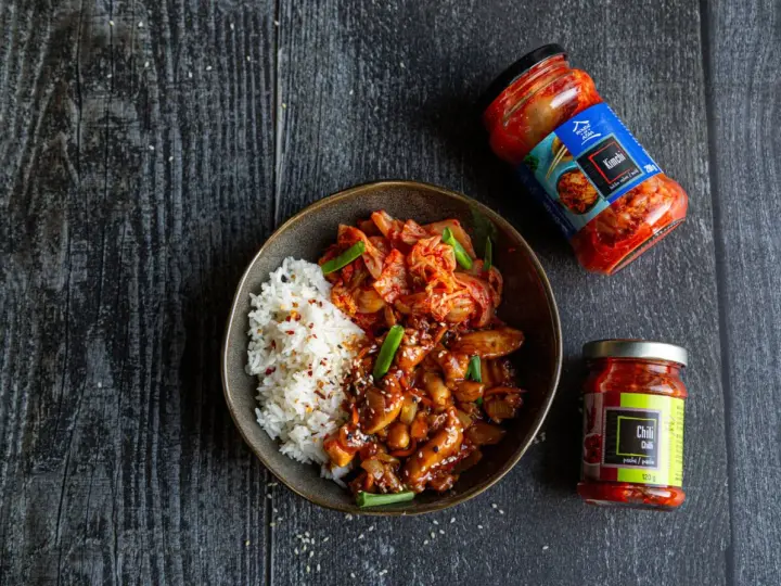 Miseczka ryżu z kurczakiem w sosie i kimchi, obok słoiczki z kimchi i pastą chili.