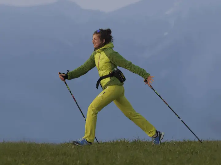 Donna sorridente pratica nordic walking su un prato. Informarsi sulle controindicazioni prima di iniziare.