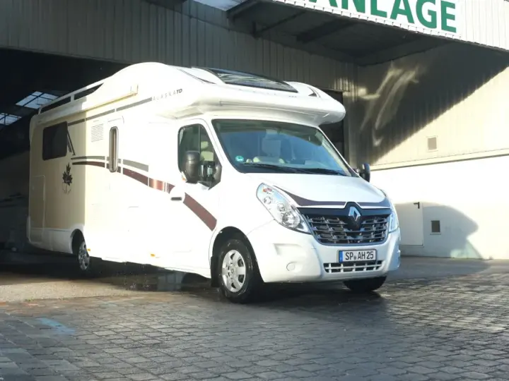 Biały kamper Alaska TD wyjeżdża z zadaszonego miejsca, gotowy na przygodę. Idealny na rodzinny camper park.