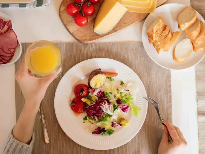 Persona disfrutando una ensalada, tomates, patata asada y un vaso de zumo, parte de su dieta intermitente 16/8.