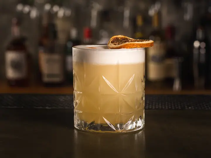 Idealny drink whisky sour z pianką i plasterkiem suszonej pomarańczy, gotowy do degustacji.