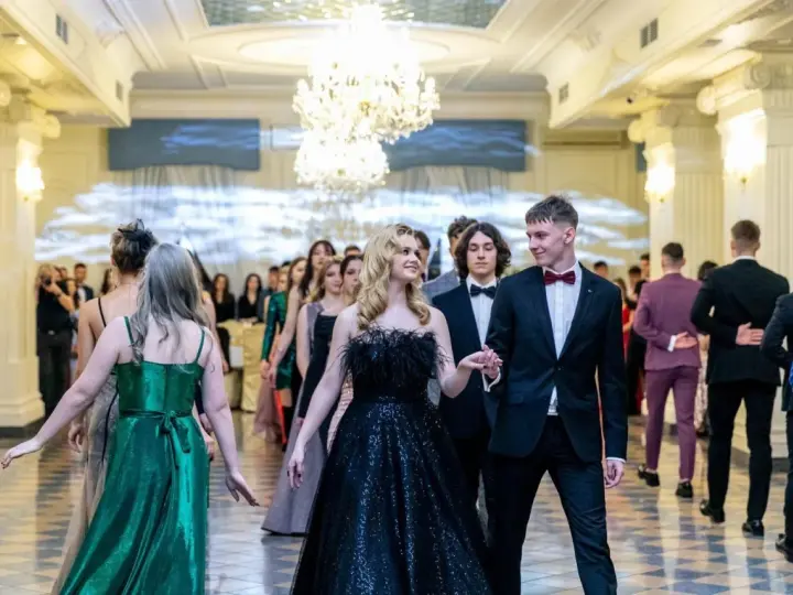 Młoda para w eleganckich strojach, ona w czarnej sukni, on w garniturze, idzie na bal studniówkowy.