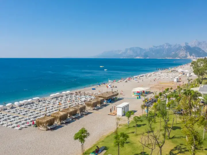 Piękna plaża z rzędami leżaków i parasoli, gdzie jest Antalya. Błękitne morze i góry w tle tworzą idealny krajobraz.
