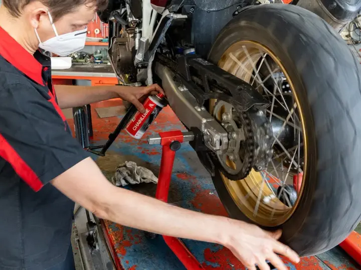 Meccanico lubrifica la catena di una moto. La pulizia catena moto ogni quanti km è fondamentale per la sua durata.