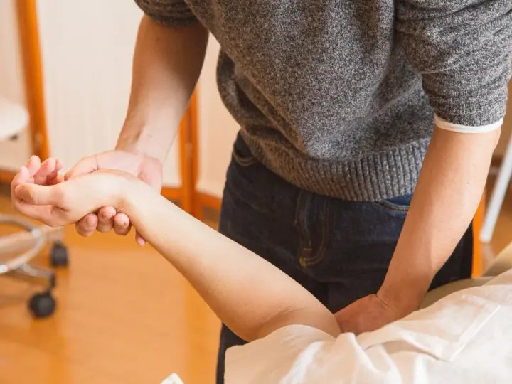 Fizjoterapeuta delikatnie masuje nadgarstek pacjenta, co jest kluczowe, kiedy zacząć rehabilitacja po operacji cieśni nadgarstka.