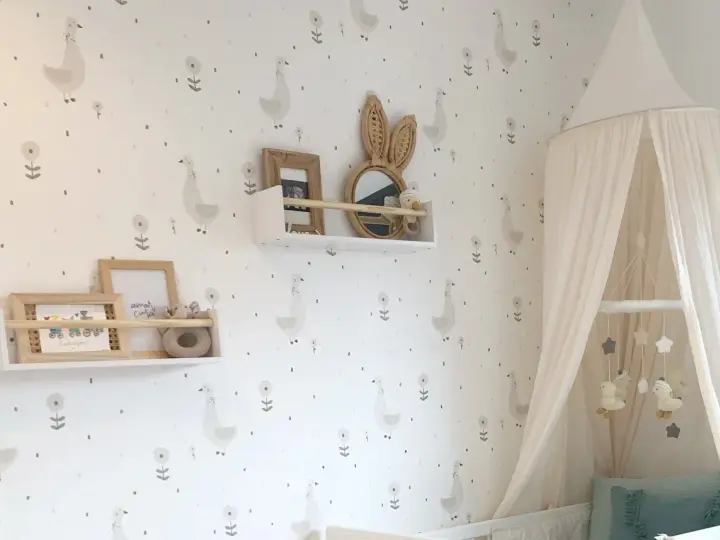 Habitaciones con papel pintado y pintura de patitos y flores. Un dosel de cama blanco cuelga sobre una cuna.
