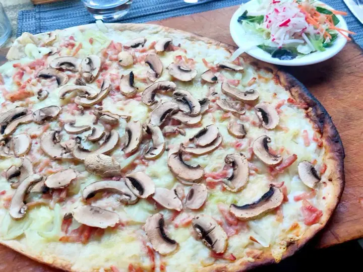 Tarta flambeada con champiñones y bacon, servida sobre tabla de madera. Una pequeña ensalada acompaña.