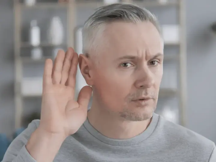 Mężczyzna z siwymi włosami przykłada dłoń do ucha, próbując usłyszeć. Czy to początek zawalu ucha?