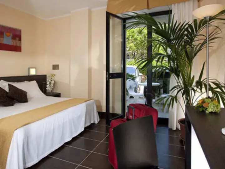 Camera accogliente al Park Hotel Kursaal Misano, con letto comodo, piante verdi e valigie rosse pronte per la partenza.