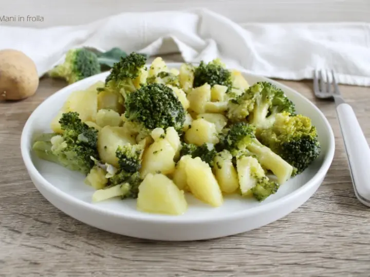 Un plato de brócoli con patatas, sencillo y saludable. Una patata entera y trozos de brócoli reposan cerca.