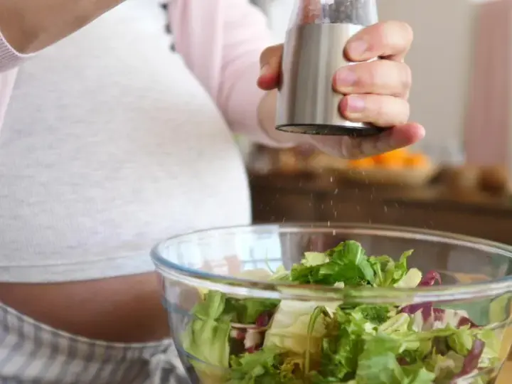 Donna incinta condisce un'insalata fresca. Ricorda come lavare frutta e verdura in gravidanza per una dieta sana.