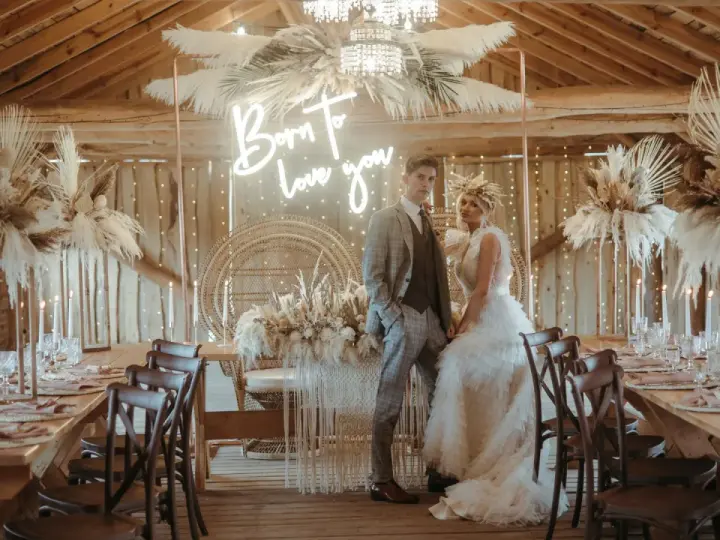 Elegancka sala weselna stodoła z parą młodą, neonem "Born to love you" i boho dekoracjami z traw pampasowych.