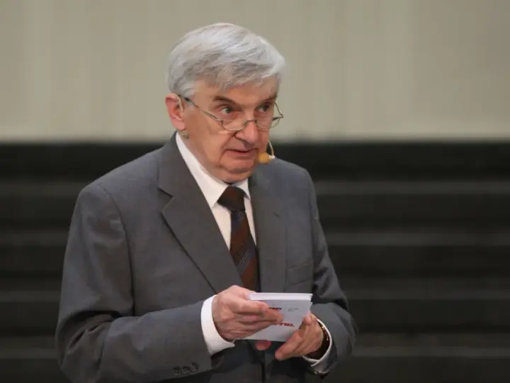 Starszy mężczyzna w garniturze, który prowadzi jeden z dziesięciu, trzyma kartkę.