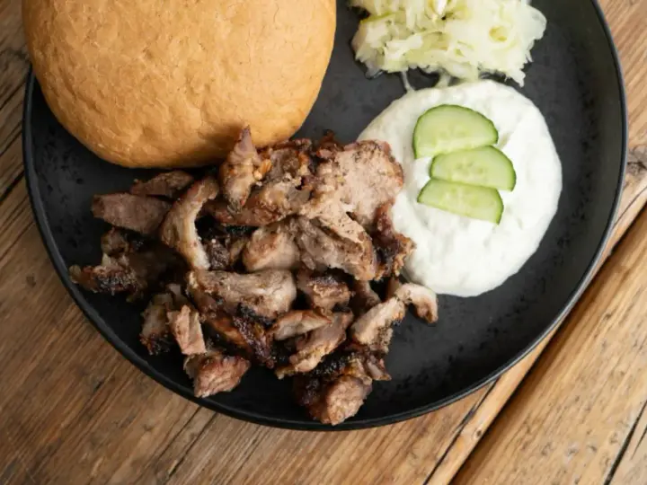 Ein Teller mit gegrilltem Fleisch, einem Brötchen, Tzatziki und Krautsalat. Perfekt für ein leckeres Gyros Rezept.