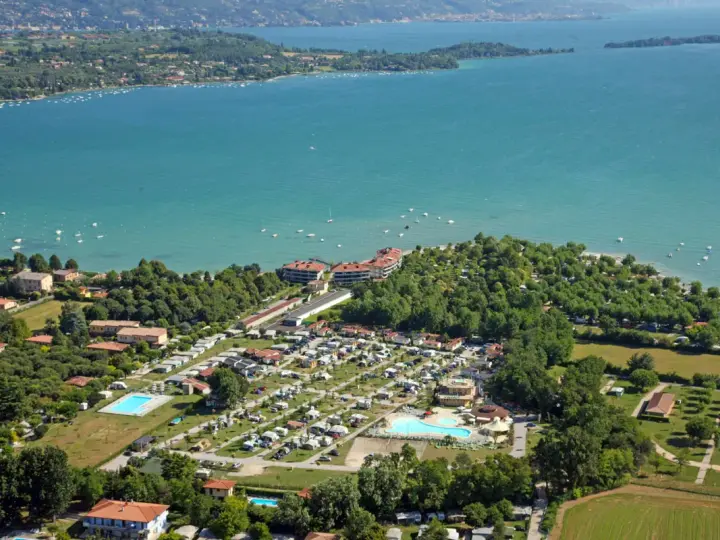 Widok z lotu ptaka na camping Baia Verde nad turkusowym jeziorem, z basenami i licznymi namiotami.