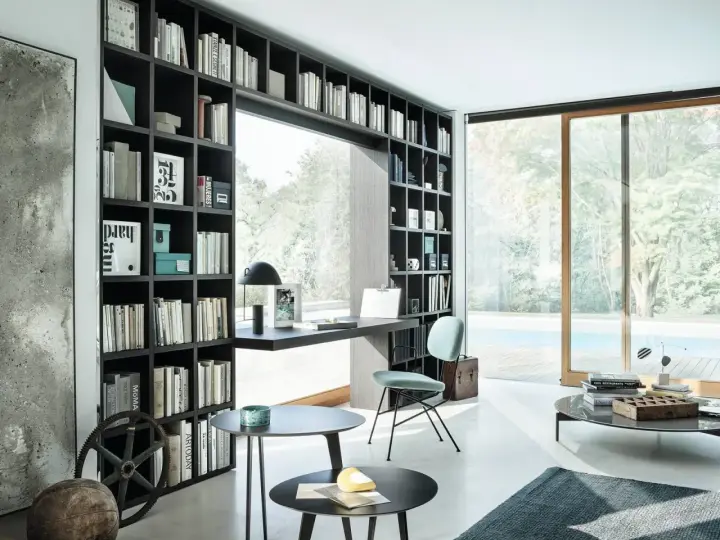 Libreria a muro con scrivania integrata, perfetta per idee stanza studio piccola. Sedia azzurra, tavolini neri e vista piscina.