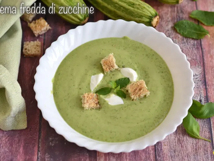 Crema fredda di zucchine servita in una ciotola bianca, guarnita con crostini, panna e menta. Fresca e invitante.