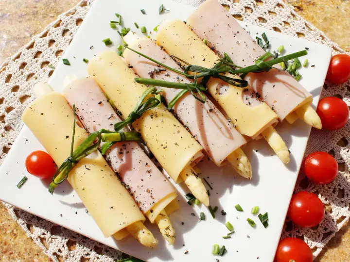 Roladki ze szparagami, zawinięte w szynkę i ser, ozdobione szczypiorkiem i pomidorkami. Pyszna przekąska.