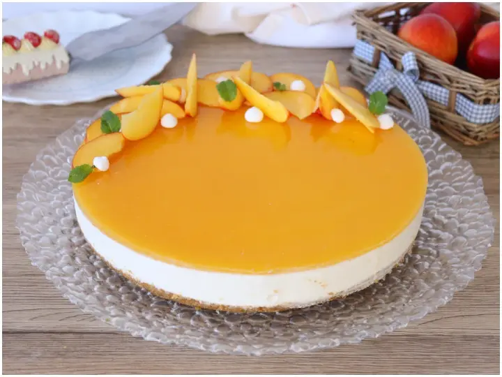 Delizioso cheesecake alle pesche con glassa lucida e fette di pesca fresca, guarnito con menta e piccole meringhe.