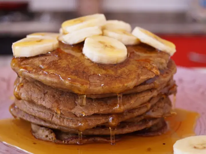 Pila de tortitas de avena y plátano, cubiertas con rodajas de plátano y sirope dorado. ¡Un desayuno delicioso!