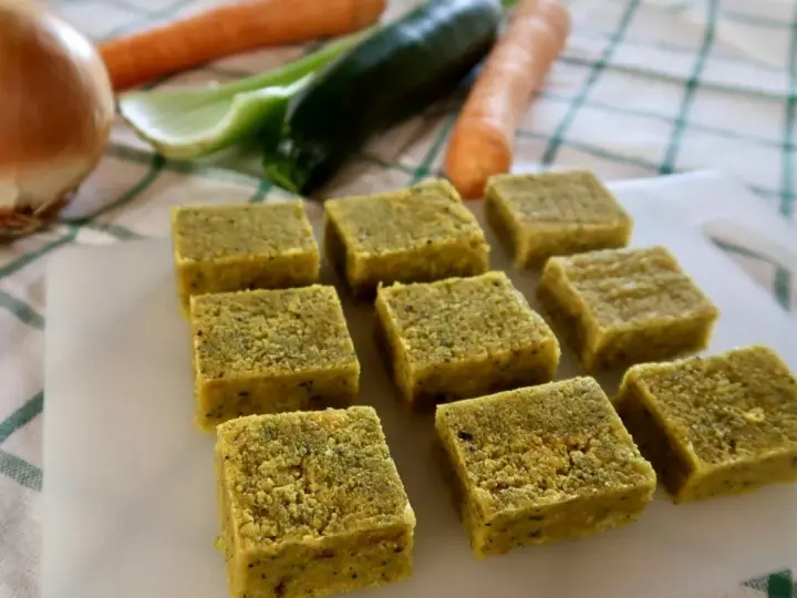 Cubetti di dado vegetale fatto in casa, pronti per insaporire le tue ricette. Sullo sfondo, ingredienti freschi come carote, zucchine e cipolla.