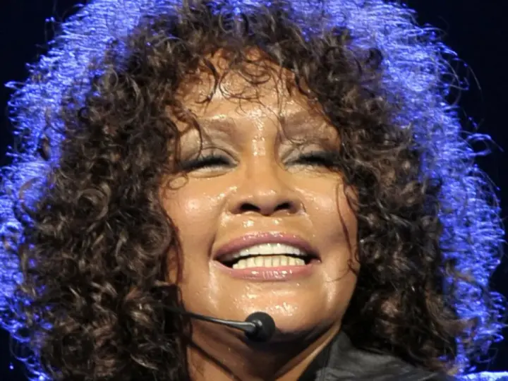 Whitney Houston z zamkniętymi oczami, w pełni emocji, pokazuje niesamowitą **skalę głosu**.