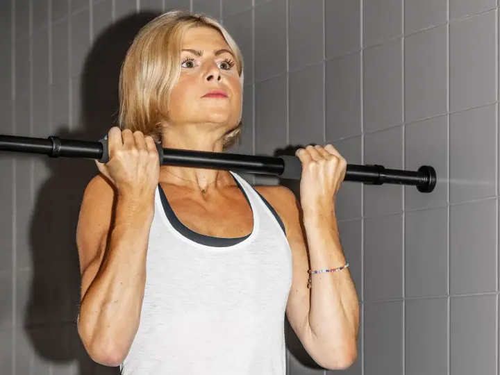 En kvinna med blont hår utför chin ups vid en stång.