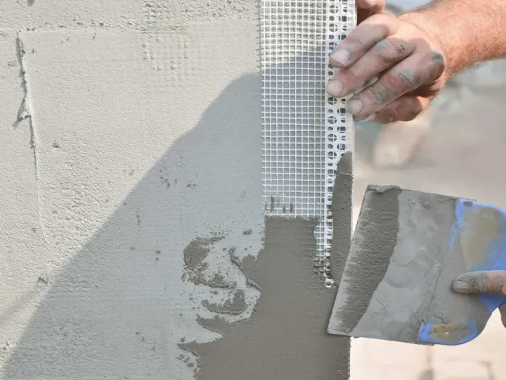 Mani esperte applicano stucco e rete per stuccare angolo muro, garantendo una finitura perfetta.