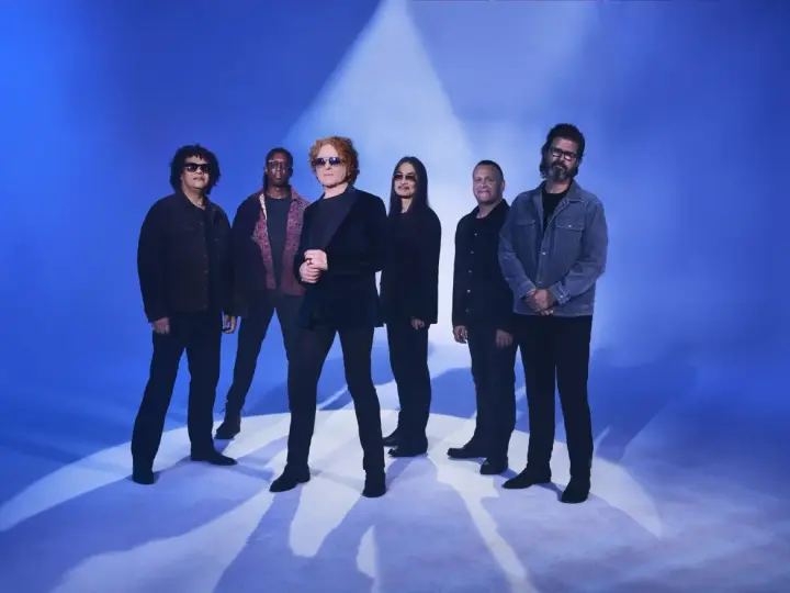 Zespół Simply Red gotowy na koncert w Polsce. Sześciu muzyków pozuje na tle niebieskiego światła.