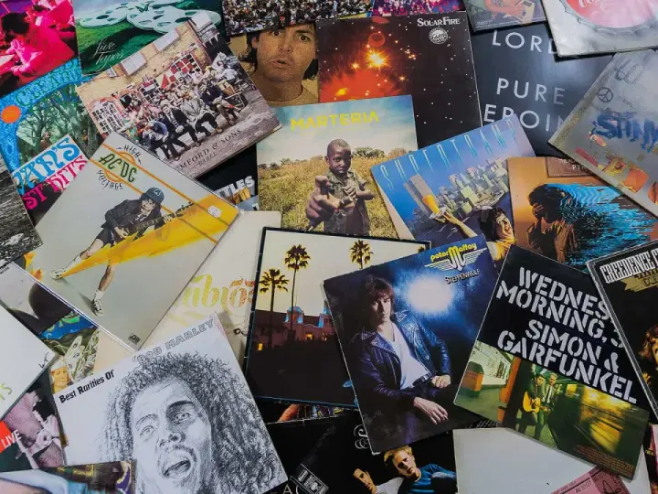 Eine bunte Sammlung von Schallplatten zeigt, welche Musikarten es gibt: Rock von AC/DC, Pop von Genesis, Folk von Simon & Garfunkel und Reggae von Bob Marley.