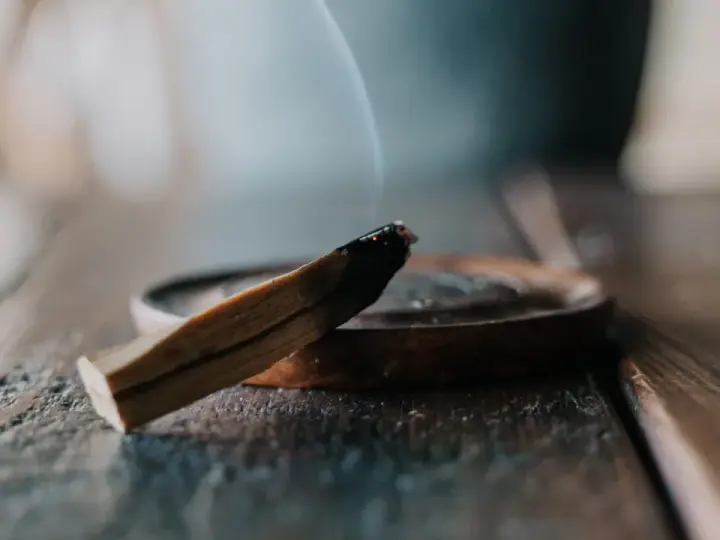 Un palo santo humeante sobre un plato de madera, parte de un ritual de limpieza.