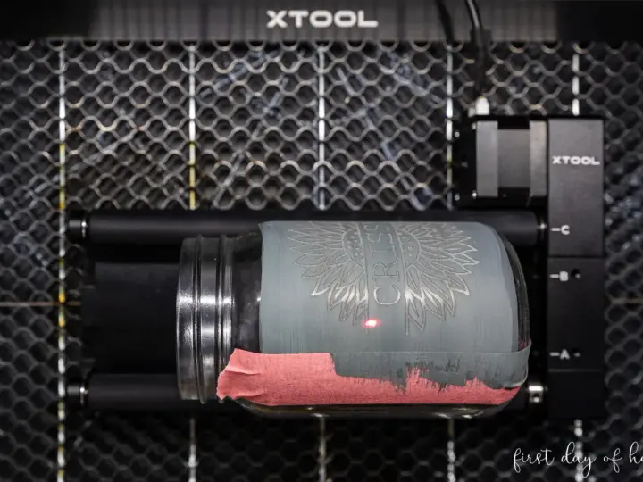 Laser engraving a jar with tempera paint. The laser is creating a sunflower design on the painted glass.