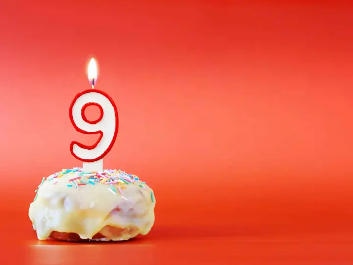En söt donut med vit glasyr och strössel, toppad med en brinnande ljusformad siffra nio. Perfekt för ett kalas för en 9-årig kille!