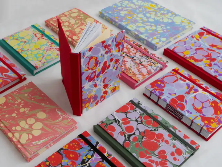 Collection de carnets aux motifs marbrés colorés, évoquant le motif Annonay. Des couleurs vives et des formes organiques se mélangent sur les couvertures.