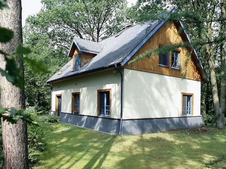 Dom otoczony zielenią, z widoczną odległością budynku od lasu. Drzewa tworzą naturalną barierę.