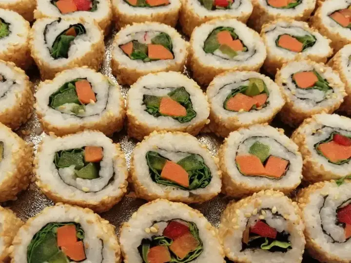 Roladki sushi z sezamem, w środku zielona sałata i pomarańczowa marchewka do sushi.