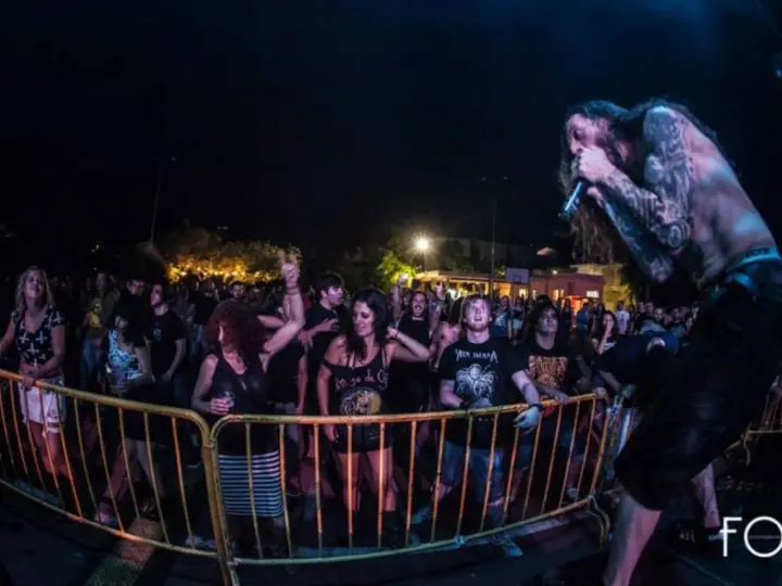 Un cantante con tatuajes canta en un concierto de charca rock. El público, animado, se agolpa tras una valla amarilla.