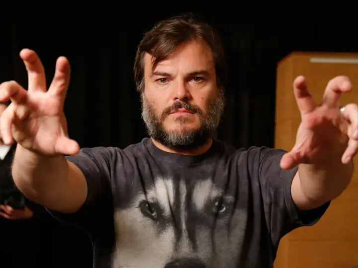 Jack Black w koszulce z wilkiem, z wyciągniętymi rękami. Ciekawe, ile lat ma Jack Black, gdy tak energicznie gestykuluje?