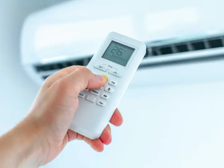 Dłoń trzymająca pilot do klimatyzatora, ustawiająca temperaturę. Ogrzewanie klimatyzatorem to komfort.