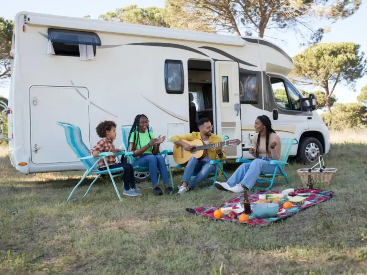 Eine Familie genießt das Camping mit Musik und Picknick vor ihrem Wohnmobil.