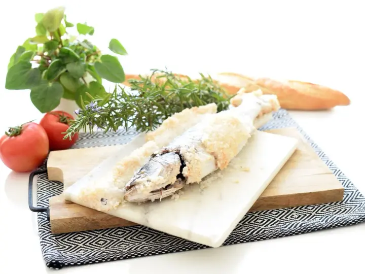 Lubina a la sal lista para servir, acompañada de tomates frescos, romero y pan rústico.