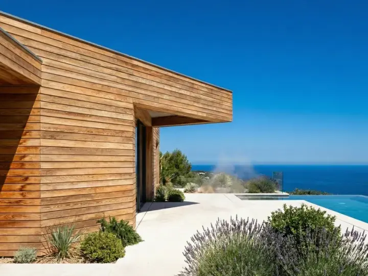 Maison moderne aux parements en bois de douglas ou pin, avec piscine à débordement et vue sur la mer.