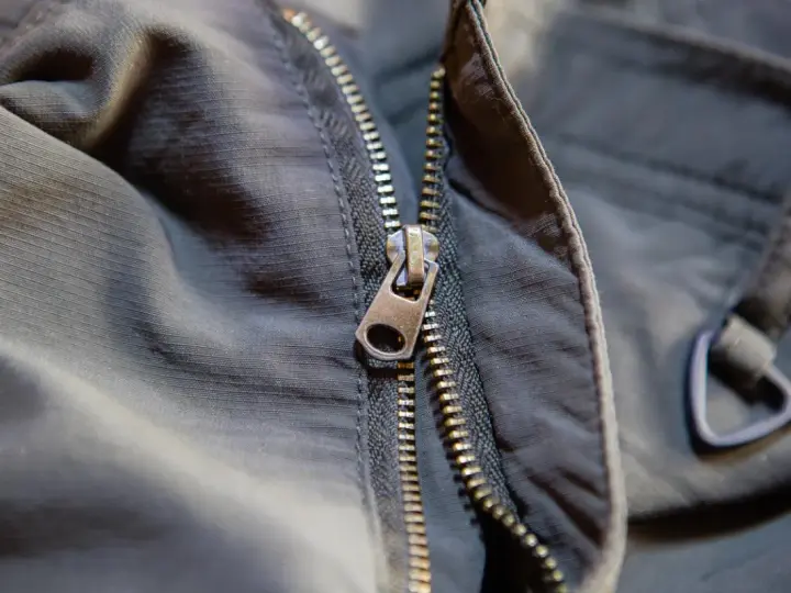 Detalle de una cremallera de chaqueta que se ha salido, mostrando el cursor metálico y los dientes.