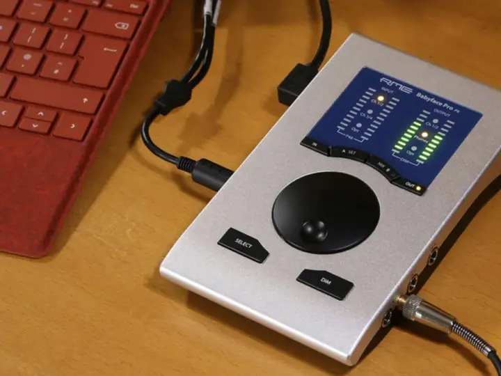 Srebrny interfejs audio RME Babyface Pro FS podłączony do czerwonej klawiatury. Idealny do mobilnego studia.