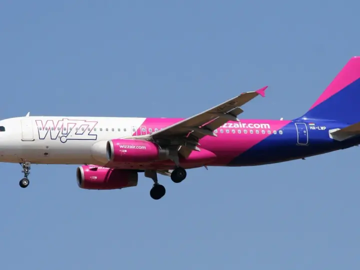 Samolot Wizz Air z różowo-fioletowym ogonem leci na tle błękitnego nieba. Sprawdź wizz discount club cena i leć taniej!