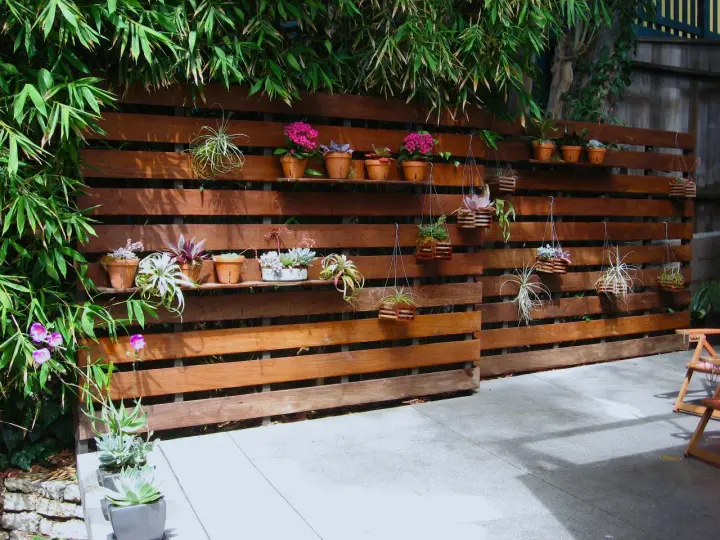 Pareti con bancali di legno ospitano piante grasse e fiori, creando un angolo verde.
