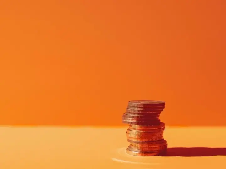 A stack of coins on an orange surface, symbolizing the business account requirements for financial growth.