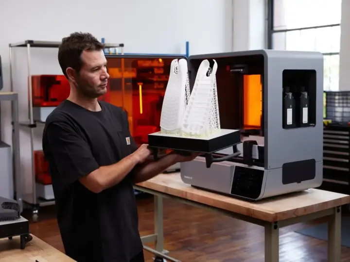 Uomo osserva due modelli architettonici bianchi appena stampati in 3D, pronti per essere rimossi dalla stampante.