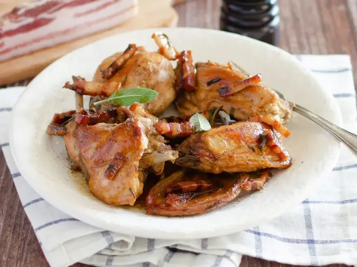 Delizioso coniglio in padella, dorato e succulento, guarnito con pancetta croccante e foglie di salvia fresca.